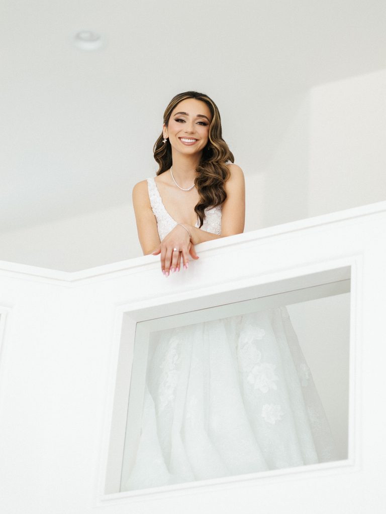 Gorgeous brunette bride leaning on white terrace barrier inside bright minimal room