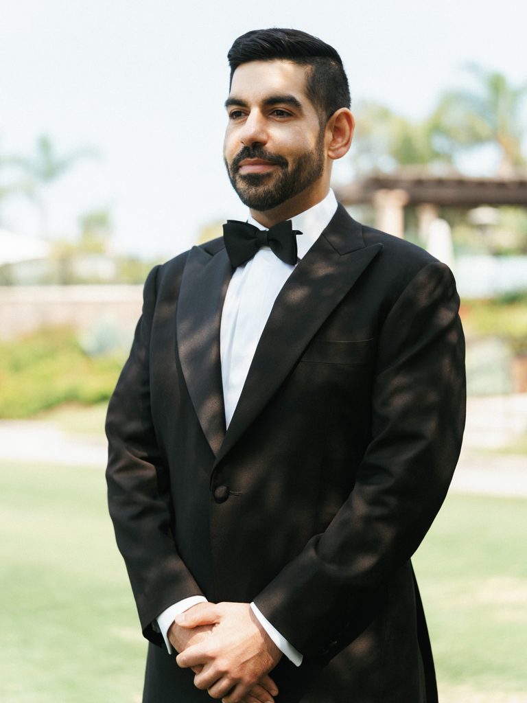 Bearded groom with styled dark hair holding hands together during wedding photoshoot