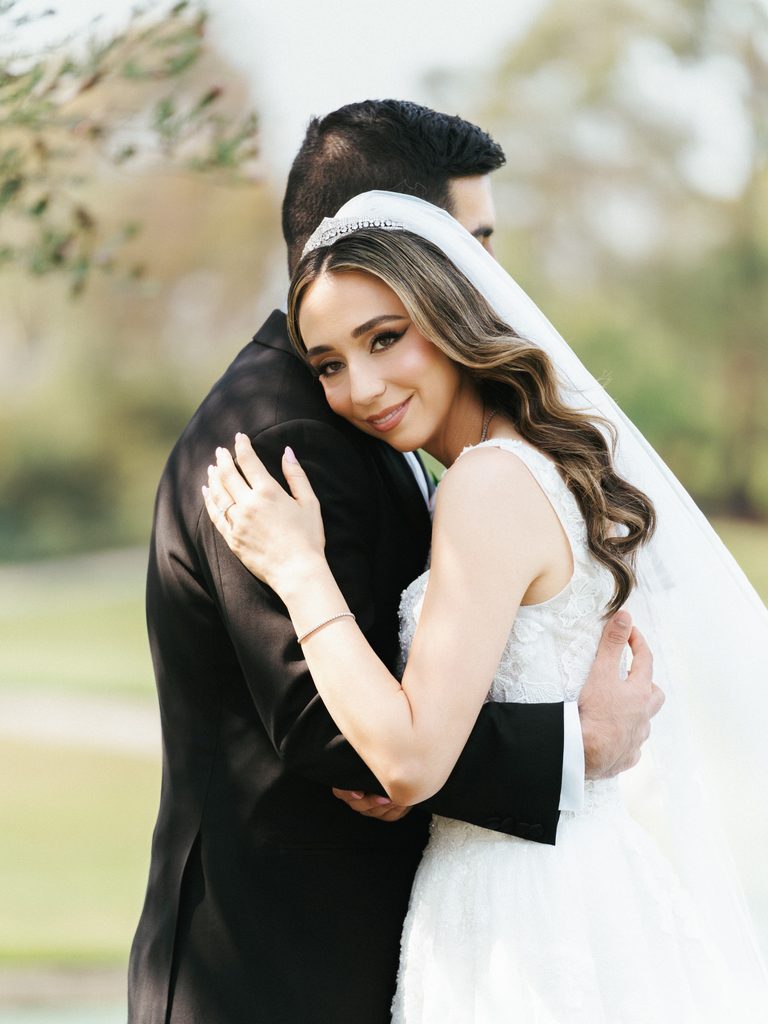 Beautiful smiling bride embracing her groom from behind during outdoor portrait session