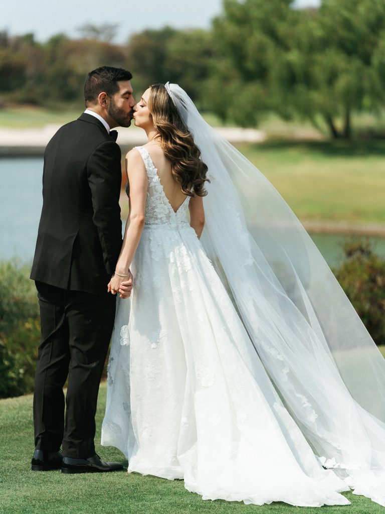 Full length portrait of newlyweds holding hands and kissing against scenic nature backdrop