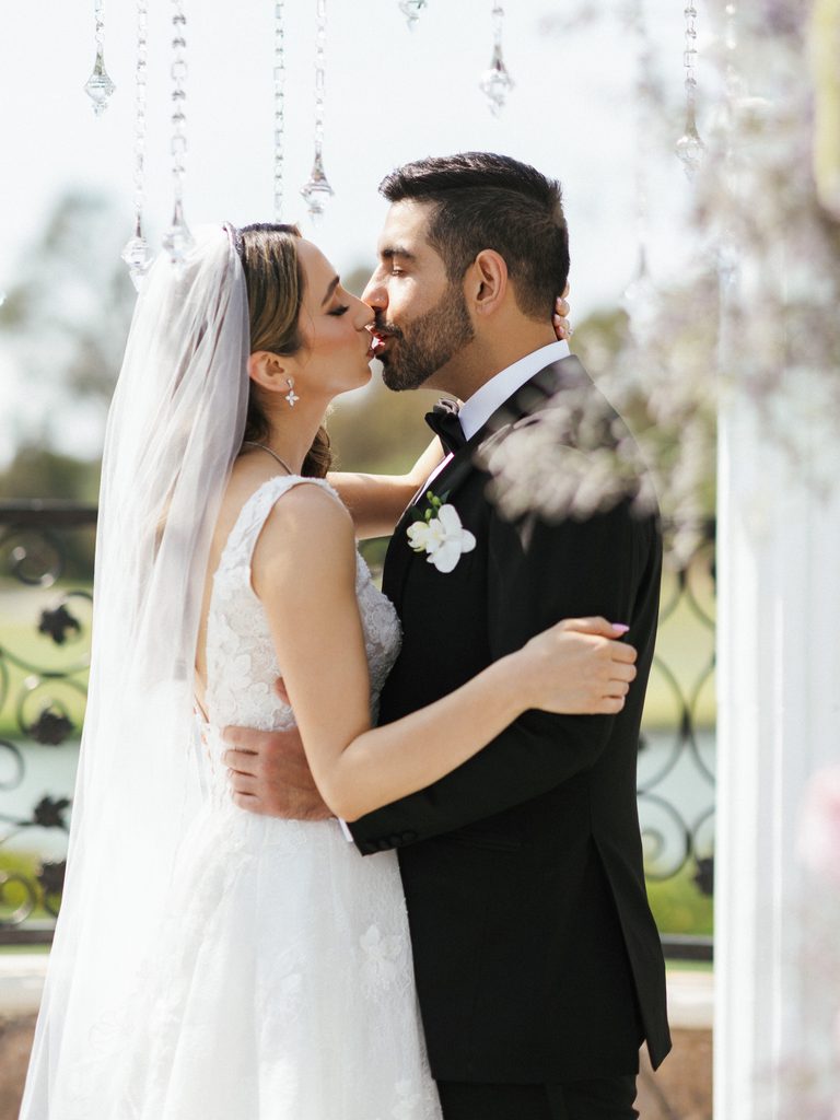 Elegant newlyweds sharing a sweet kiss outdoors during luxury backyard mansion wedding