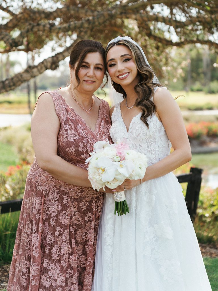 Tender family moment outdoors with smiling bride and her proud mother looking at camera