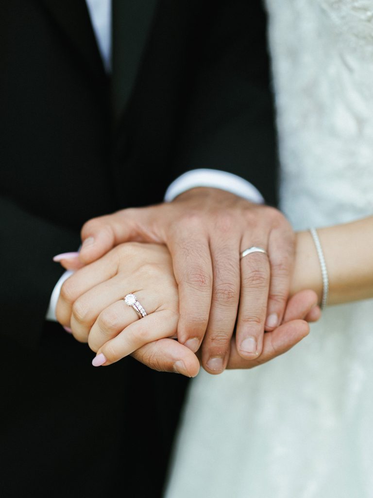 Macro shot of newlyweds hands intertwined with silver wedding bands visible