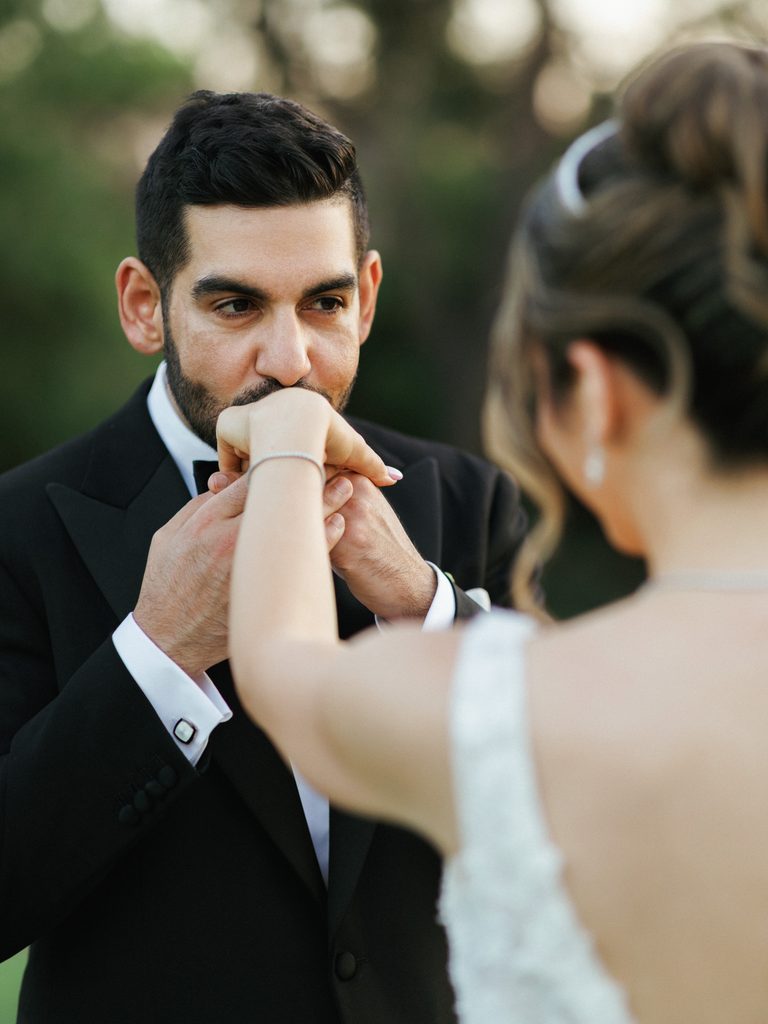 Charming groom kissing bride hand with closed eyes during outdoor portrait session