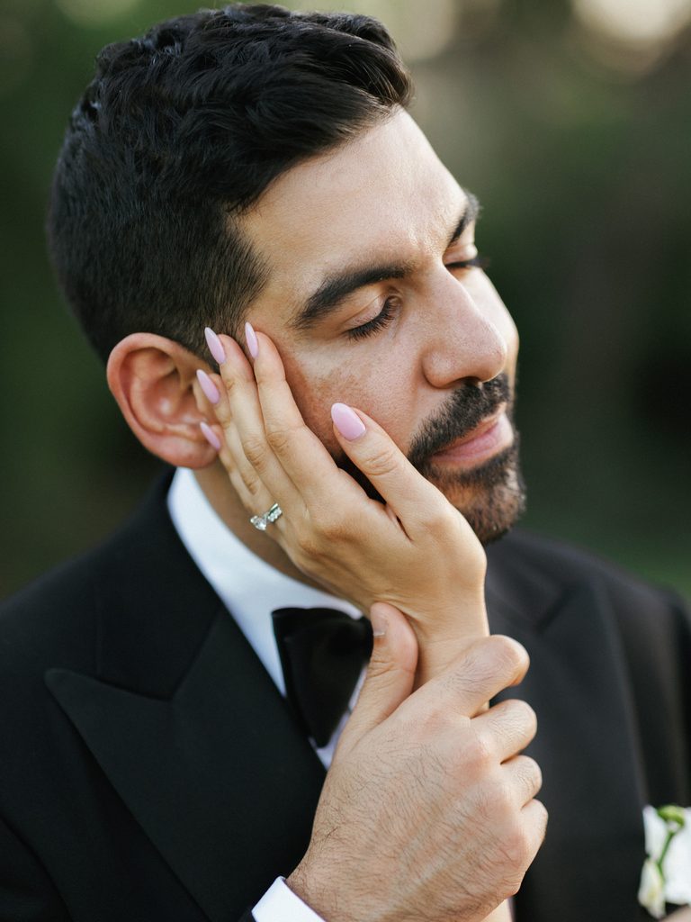Beautiful profile of groom with bow tie enjoying a sweet gesture from his wife outdoors