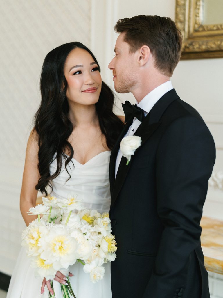 Beautiful brunette bride with wavy hair admiring groom during indoor wedding photoshoot