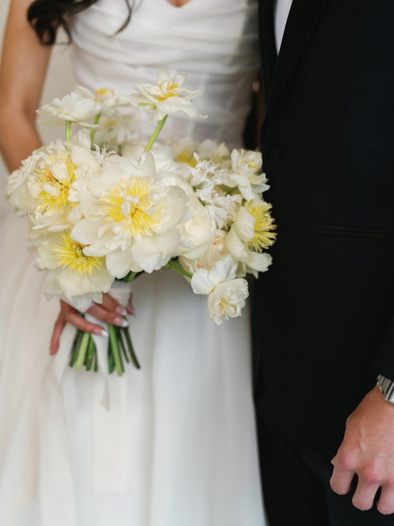 Macro shot of lush summer bridal flowers with bright yellow centers next to groom black suit