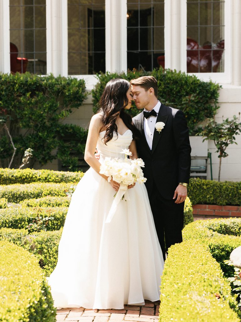 Beautiful bride in strapless white gown leaning towards groom in classic black tuxedo