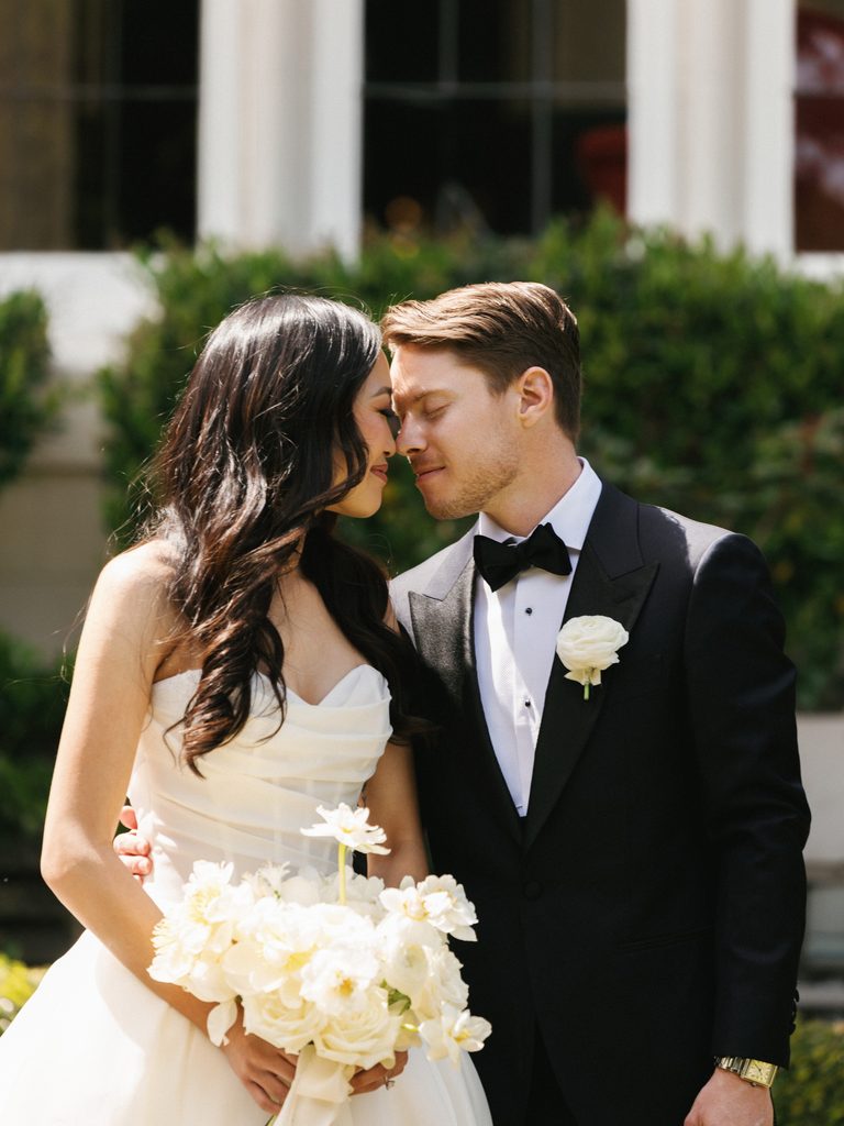 Beautiful brunette bride and handsome groom posing together with lush creamy roses