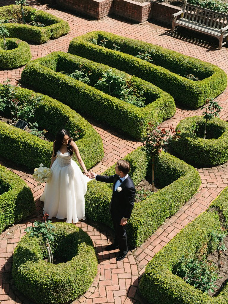 Stunning aerial perspective of bride and groom holding hands in luxury manicured garden