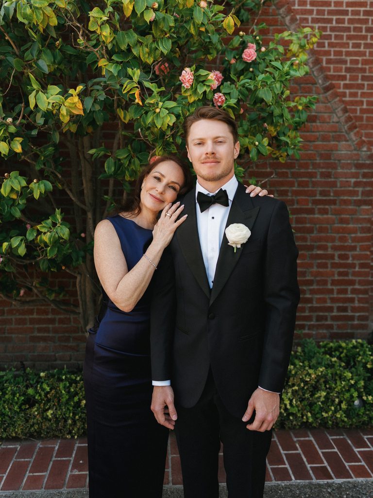 Proud mother of the groom holding son arm near red brick building exterior