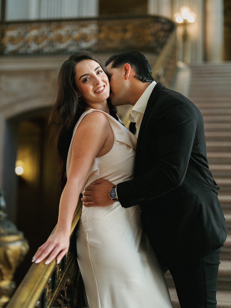 Groom kissing smiling bride on neck during winter city hall wedding photoshoot