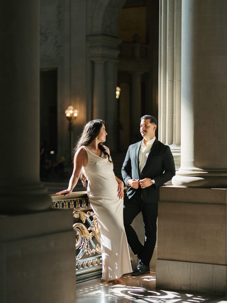 Winter wedding couple posing near columns inside historic city hall with dramatic sunlight