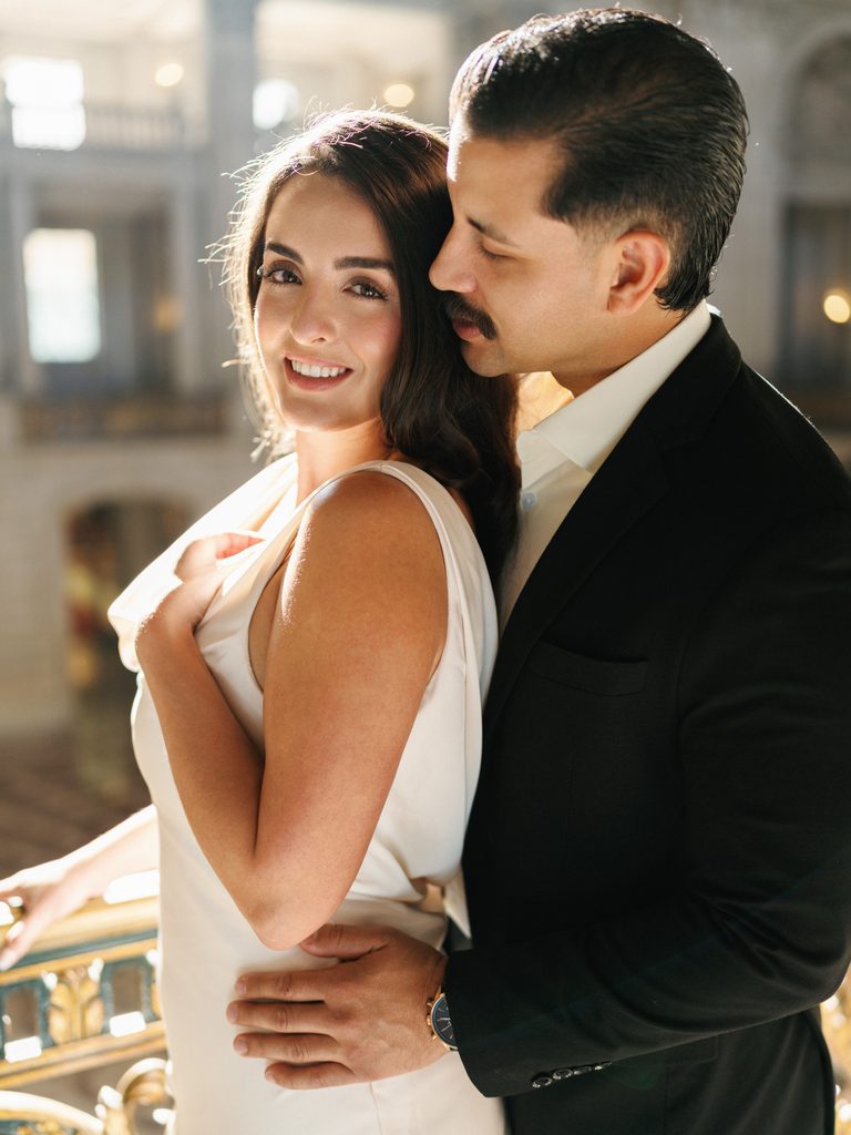 Groom hugging smiling bride from behind during luxury winter wedding indoor photoshoot