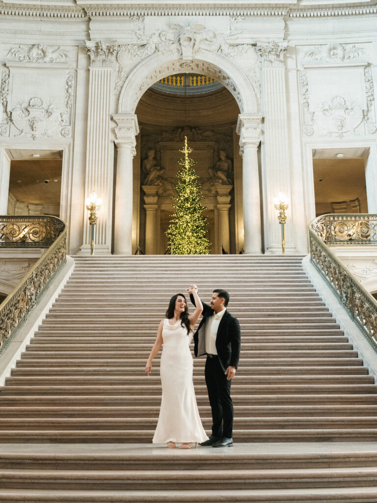 Winter wedding couple dancing on grand marble stairs with decorated Christmas tree background