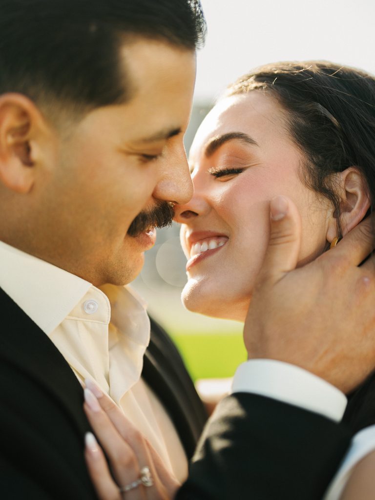 Groom gently holding smiling brides face during sunny California winter wedding photoshoot