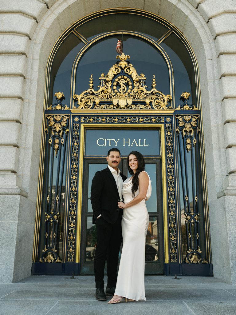 Winter wedding couple posing in front of iconic golden City Hall entrance gates