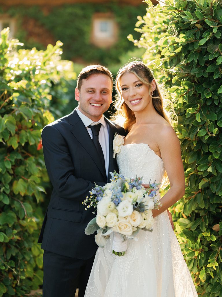 Smiling bride with long wavy hair holding white bouquet outdoor at luxury vineyard wedding